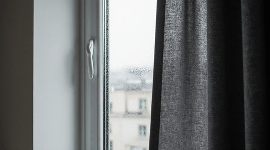 Rideau occultant gris foncé installé près d’une fenêtre avec légère condensation sur le vitrage.