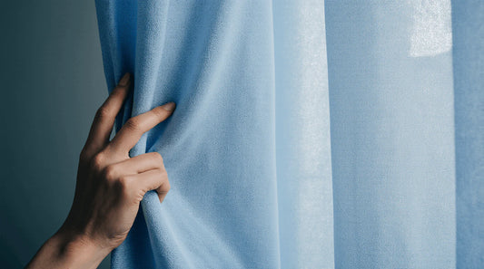 Texture en gros plan d’un tissu occultant triple couche devant une fenêtre en lumière naturelle.