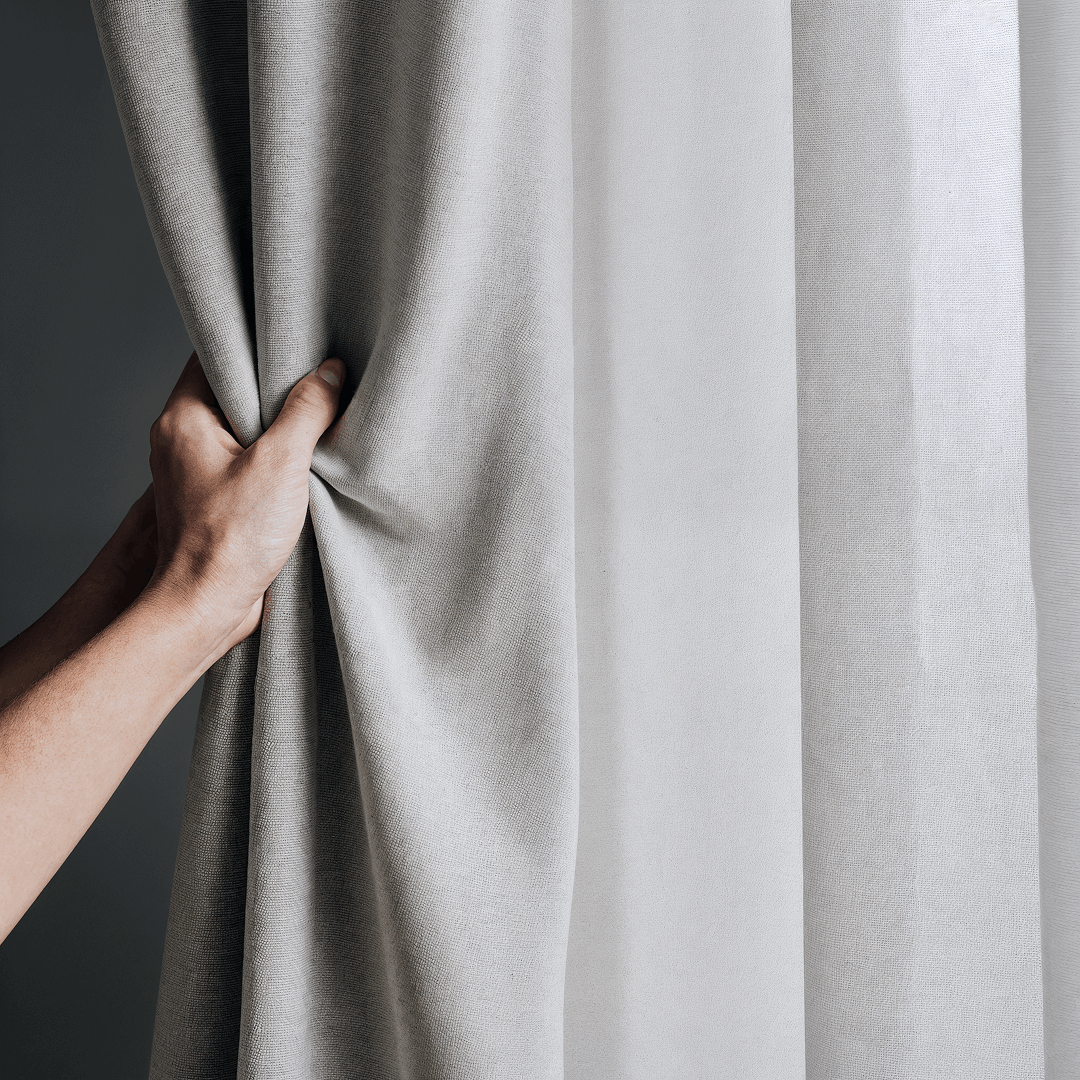 Main tenant un rideau en tissu clair, montrant la texture et l’épaisseur du textile
